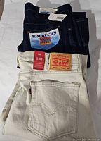 Two pairs of jeans stacked: top - Levi's beige tie-dye jeans, bottom - dark blue Sears Roebucks jeans with original tags