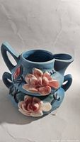 Side view of the creamer showing blue pottery with raised pink flowers and handle