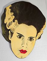 Front view of painted wooden wall hanger shaped like the Bride of Frankenstein's head with detailed facial artwork.