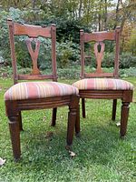 Front view of two antique wooden chairs with carved backs and striped upholstered seats placed on grass outdoors.