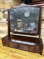 Antique bow front dressing mirror showing front view with mirror surface, three drawers, and wooden construction.