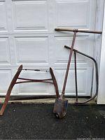 Photo of an antique post hole digger with wooden T-handle and rusted metal digging heads, two rusty hand saws with wooden handles, one with a bow frame and tension spring, the other with a curved blade holder.