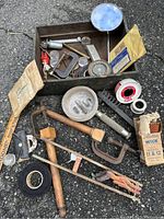 Top view of box containing assorted vintage metal tools, clamps, saw, mirror, magnifying glass, measuring tape and small reels.
