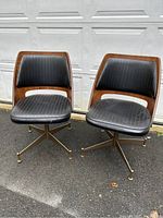 Pair of mid century swivel chairs side by side with bentwood backs and black upholstery seats on metal swivel bases with brass-capped feet.