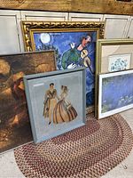 Five framed art pieces leaning against a cabinet including a large colorful Chagall print, a vintage couple artwork in blue frame, and other varied prints including Monet theme.