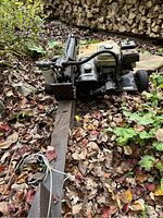 Angled side view of entire log splitter on leaf-covered ground showing frame, wheels, engine, hydraulic beam.