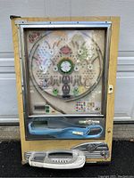 Front view of the vintage Nishijin Pachinko game machine showing the wooden frame, glass front, and the playfield inside with metal pins and scoring pockets.