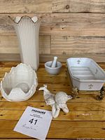 Overview of porcelain items including vase, shell dish, mortar and pestle, figurine and soap dish on metal stand arranged on wooden surface.
