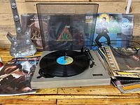 Panasonic LAB-89 turntable with vinyl record and various album covers behind it with stack of books to right and silver hand decor in the background.