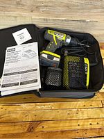 Complete Ryobi 12V cordless drill kit laid out in black carrying case including drill, two batteries, charger, and instruction manual.