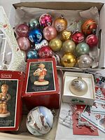 Box with vintage Shiny Brite glass ball ornaments in red, gold, blue, pink, green, silver colors with various holiday painted designs, plus boxed Schmid Hummel figurines and additional decorations.