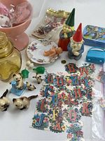 Wide view of lot showing various small porcelain cats, two garden gnome figurines with green and red hats, small decorative plates, alphabet letter magnets scattered on the surface, and other assorted small figurines including a dog holding a letter and small green leaf shapes.