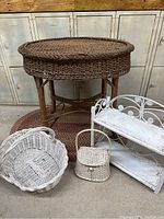 Photo showing the oval wicker table with wooden legs, white two-tier accent shelf with decorative scrollwork, and three woven wicker baskets in different shapes and sizes.