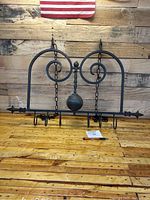 Front view of the wrought iron hanging pot holder, showing scroll design, chains for hanging, and hooks at the bottom.