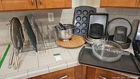 Multiple metal bakeware pans, cooling racks, colanders and wood lazy susan displayed on kitchen countertop