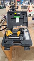 Open hard plastic carrying case with Bostitch air nailer and several packs of nails inside, displayed on a workbench.