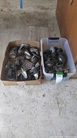 Two boxes containing multiple used cart wheels of various sizes and conditions, some with rust and dirt.