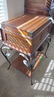 Side angled photo of wooden end table with metal legs showing drawer top and carved panel details with metal corner braces.