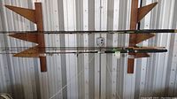 Fishing poles mounted on wooden rack against corrugated metal wall. Clear view of cork and synthetic handles and metal line guides.