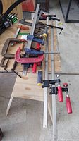 Photo of multiple large clamps laid out on a wooden workbench including red Husky clamps and Irwin clamps with metal bars and screw handles