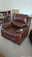 Brown leather recliner angled view showing cushioned seat, armrests, and back with visible handle on side.