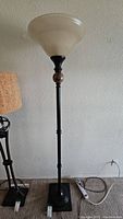 Full view of the tall black metal floor lamp with marble accent near the top, frosted glass wide flared shade, and square base.