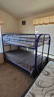 Full side view of the blue metal framed bunkbeds showing both bunks and mattresses