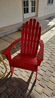 Red wooden Adirondack chair with slatted back and wide armrests, painted red, shown on patio.