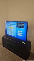 Television powered on showing on-screen menu, placed on black TV stand