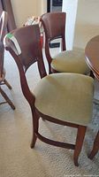 Side and front angle of two tall wooden dining chairs with fabric seats and studded trim on the backrest.