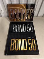 Photo showing the Bond 50 Blu-ray box set with James Bond figure silhouettes on the cover, and two hardcover Bond 50 books underneath.
