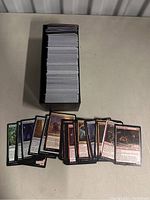 Black card box filled with many Magic: The Gathering cards, some cards fanned out in front of the box showing various card faces.