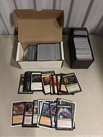 Two open boxes, one white and one black, displaying Magic: The Gathering cards with some cards spread out in front showing a variety of card types including creatures and spell cards.