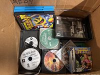 Cardboard box with upright blue PS4 cases, a black PS2 case, loose discs and one GBA boxed cartridge