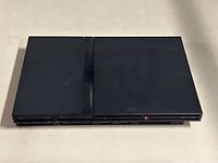 Top view of black PlayStation 2 Slim console showing two-part top panel with light scratches and PlayStation branding.