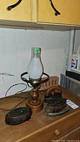Photo of three antique cast iron flat irons marked 'Brockville' and a vintage wooden and metal lamp base without its globe shade