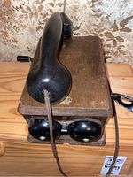 Front view showing black handset with cloth-wrapped cord and wooden box.
