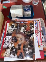 Photo of Blue Jays 25 Seasons yearbook with additional newspapers and magazines underneath on red table