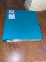 Blue binder labeled 'Baseball Cards' on a sticker, shown closed and lying on wooden floor