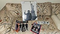Photo showing Beatles USA Ltd book, Beatles Reunion leaflet, and 20x16 poster print of John Lennon with Statue of Liberty on a floral couch.