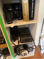 Carl Wetzlar 7x35 binoculars with case and original box on a shelf, Panasonic cassette recorder with headphones below them