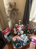 Photo showing metal lawn wind chime ornaments and various pots with faux flowers and greenery, along with miscellaneous holiday decorations on floor by window.