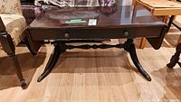 Front view of the Gibbard mahogany coffee table showing double drop leaf design, central drawer with two pulls, and curved legs with brass feet caps.