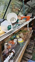 Various plastic and terra cotta planters, some with holes and signs of use, displayed on greenhouse shelving.