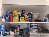 Shelf display of assorted household cleaning and maintenance products including liquids, sprays, rags, tape, and small containers.