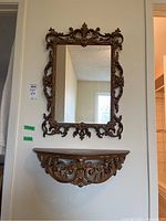 Straight-on photo of mirror above wall shelf, showing ornate design and finish.