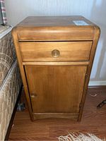 Front view of wooden nightstand showing drawer and cabinet door with circular brass knobs.