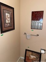 Three wall-hanging art pieces in a bathroom corner: two framed prints and one metal wall art.