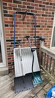 Front view of three snow shovels showing white plastic scoops and blue black handles leaning against the brick wall.