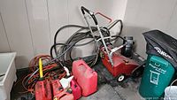 Overview showing Duramark snow blower, two red jerry cans, multiple hoses and extension cords on floor against wall